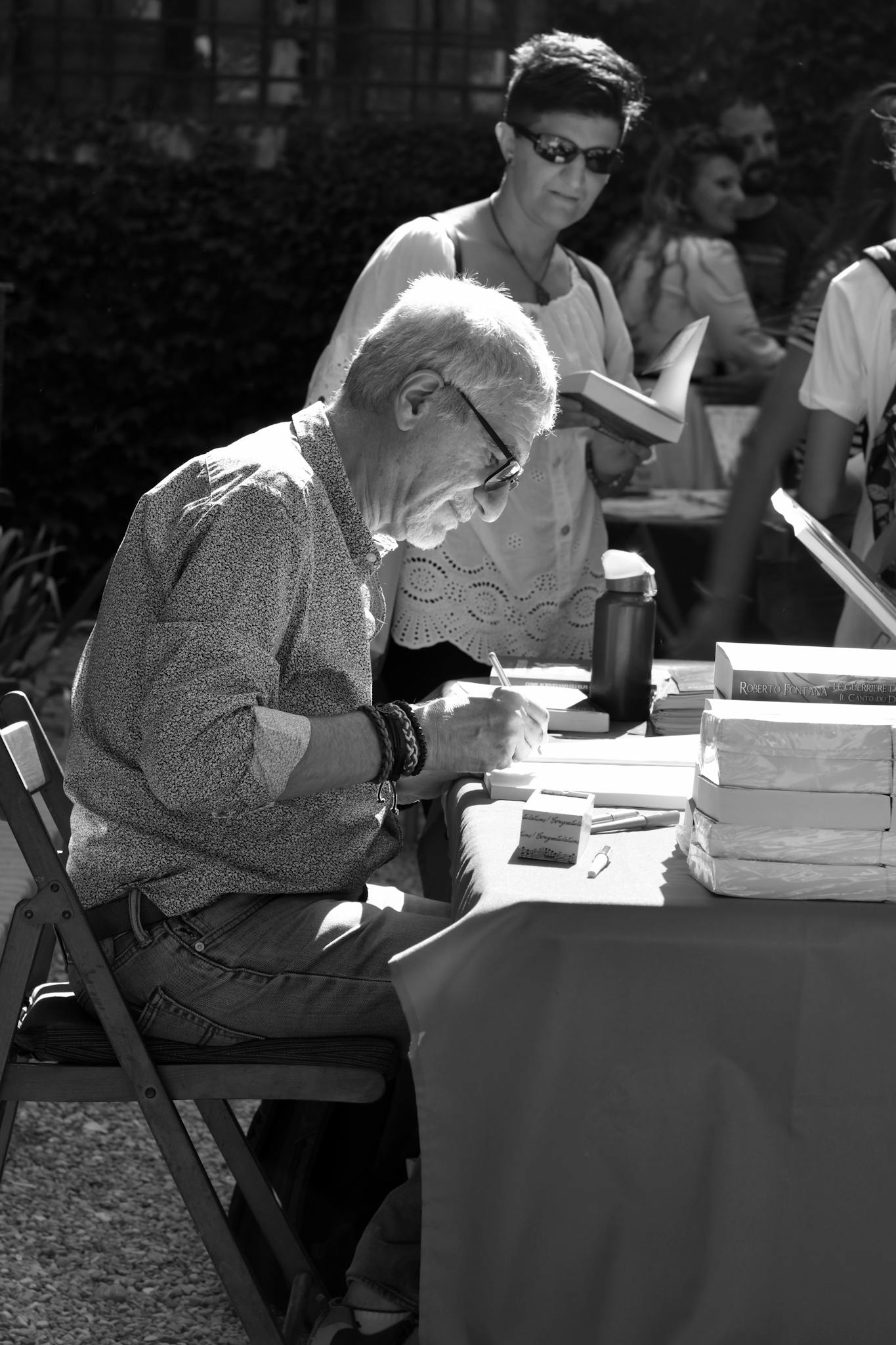 An elderly man signing books at an outdoor event in Grazzano Visconti, Italy.