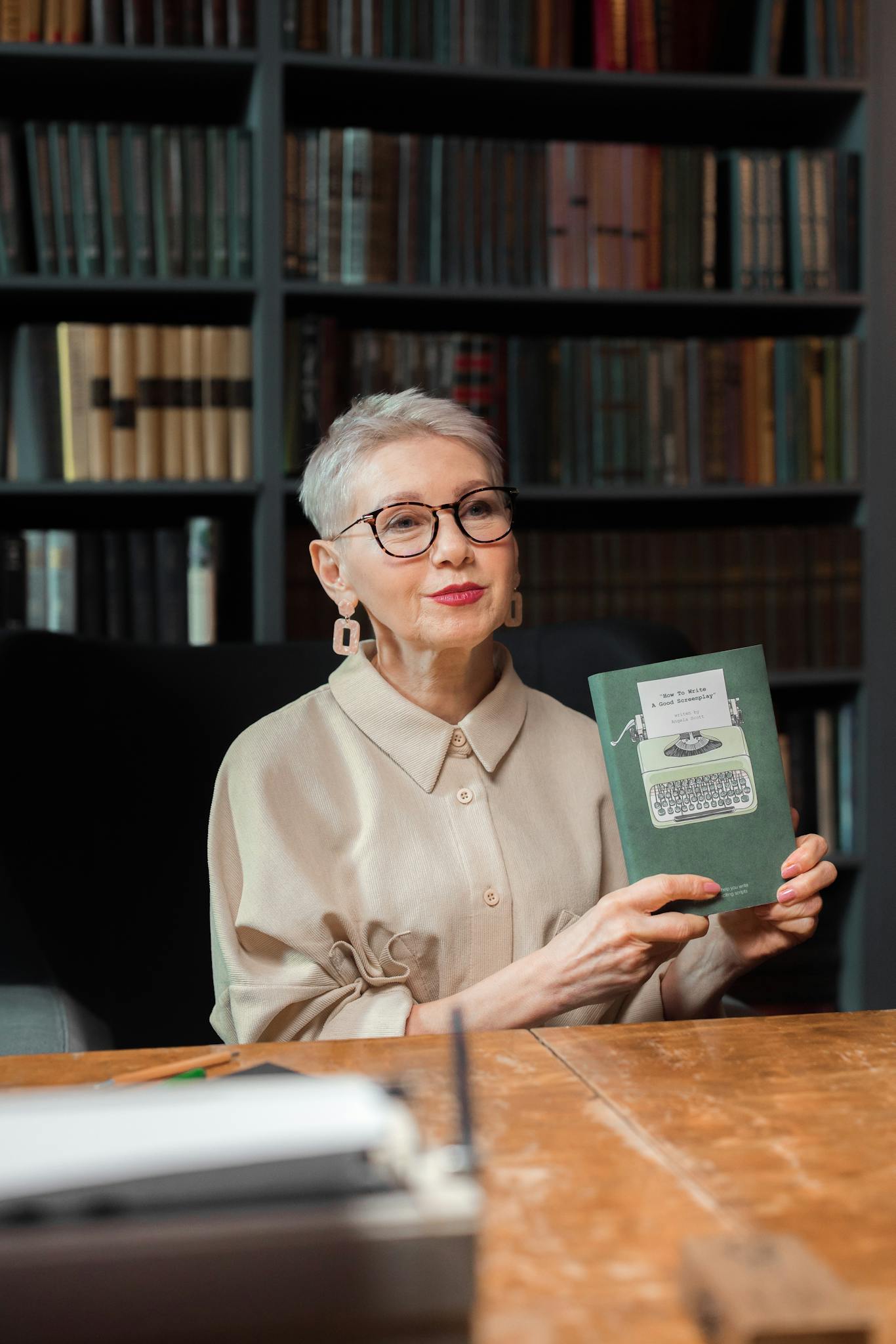 Elderly woman with short hair holding a book, sitting in a library, creating a scholarly ambiance.