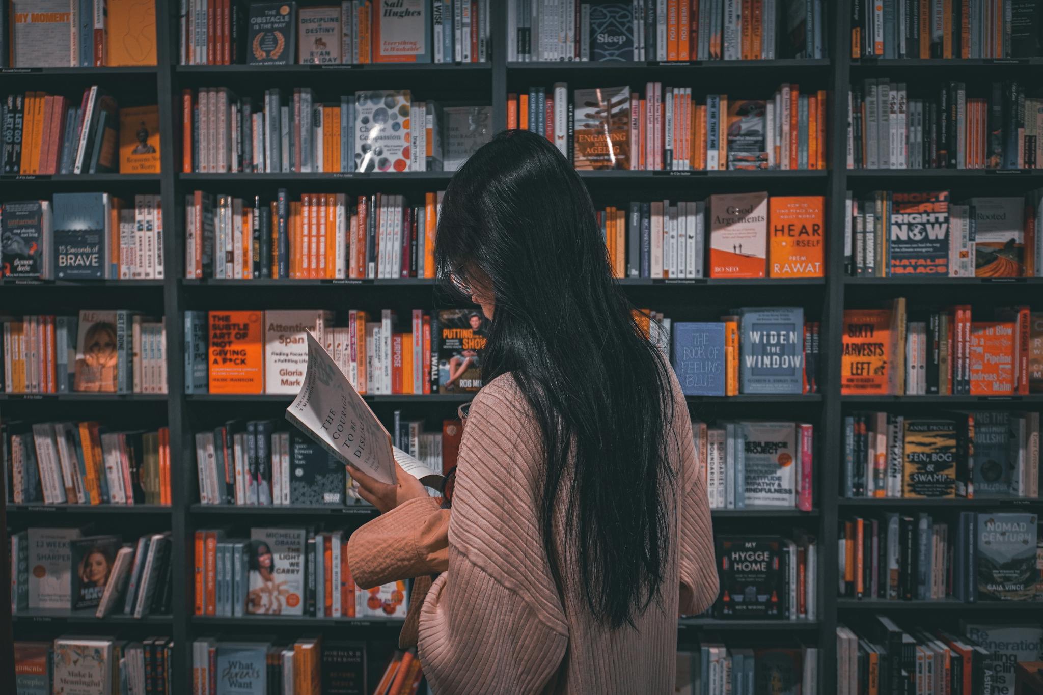 Young woman engrossed in a book amidst colorful bookstore shelves.